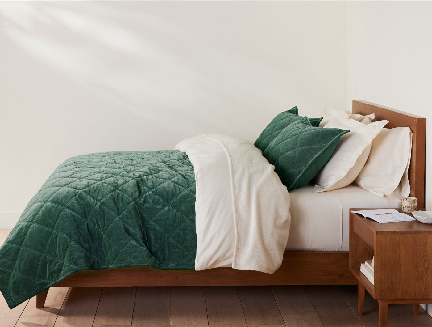 Coyuchi Velvet pillow sham in forest green, styled on a made bed with matching quilt.