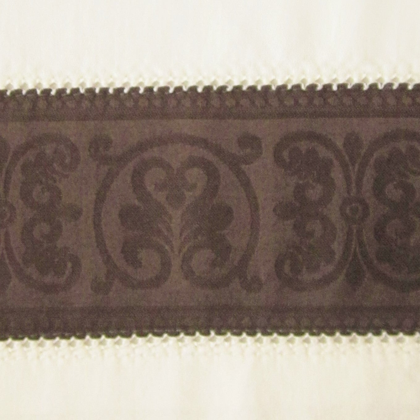 Close-up of chocolate jacquard medallion border trim on ivory linen pillow sham.