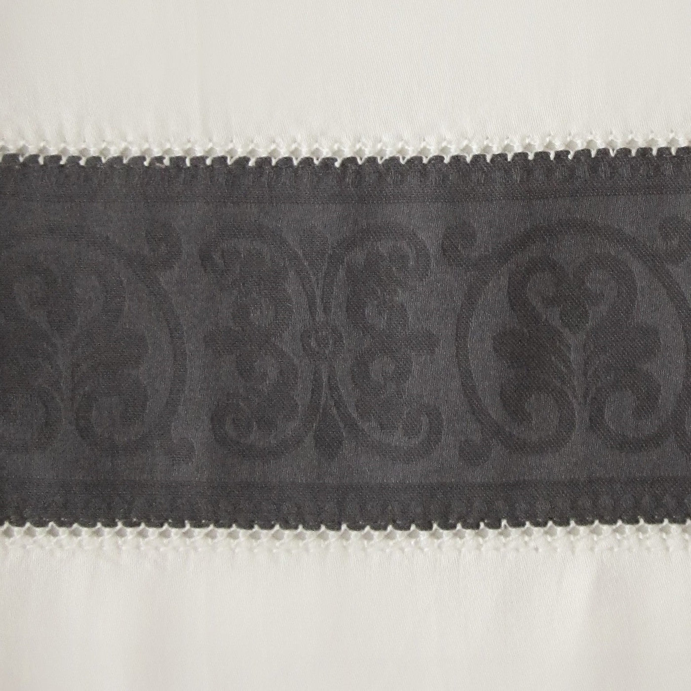 Close-up of charcoal damask border with scalloped trim on ivory linen flat sheet.