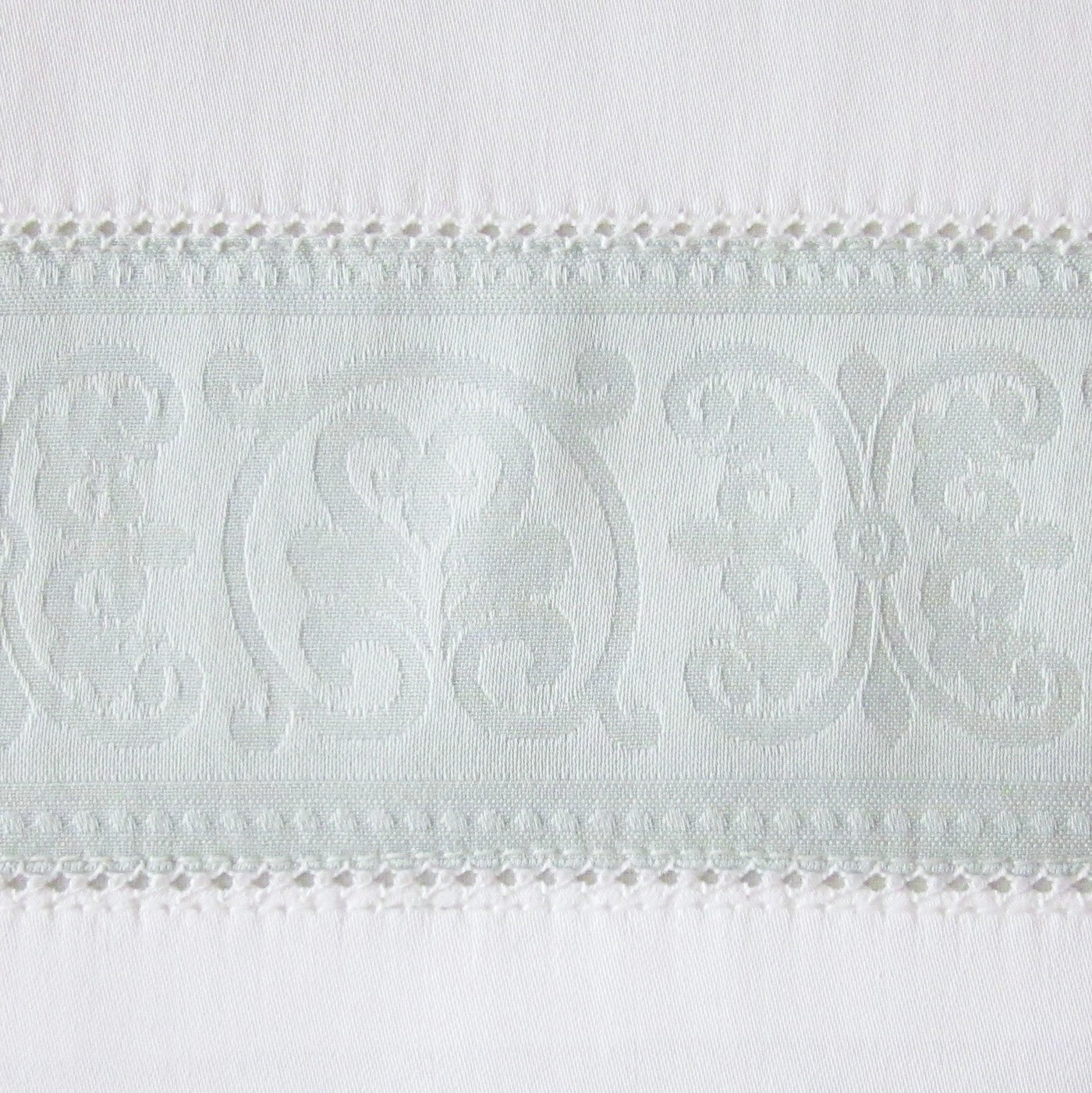 Close-up of Venice flat sheet's jacquard medallion border with crochet lace trim in white.