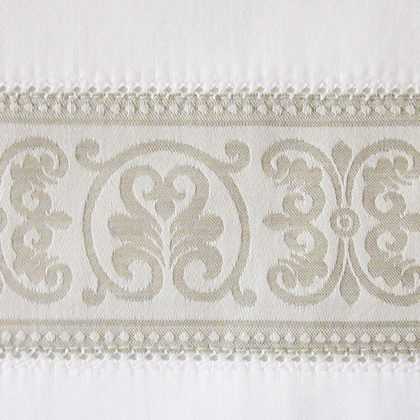 Close-up of taupe damask border with scroll motifs and beaded trim on ivory cotton.