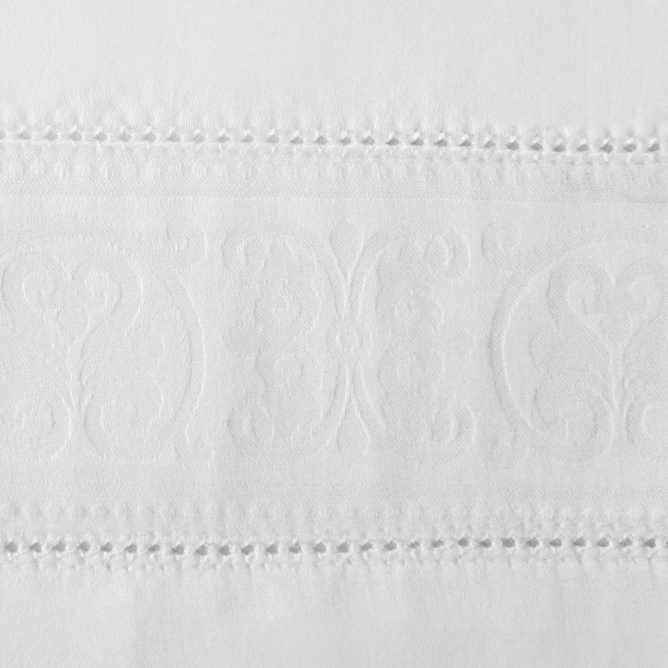 Close-up of embroidered medallion border with hemstitched trim on white cotton.