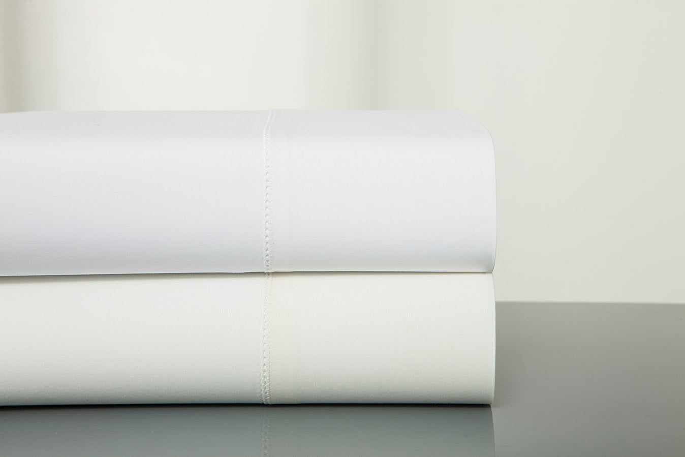 Close-up of folded white and ivory Home Treasures Villa yardage stacked on a grey surface.
