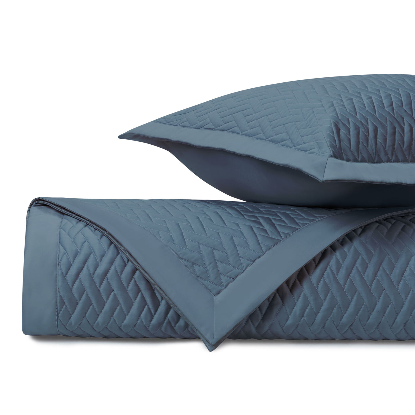 Close-up of slate blue quilted coverlet with geometric diamond stitching pattern.