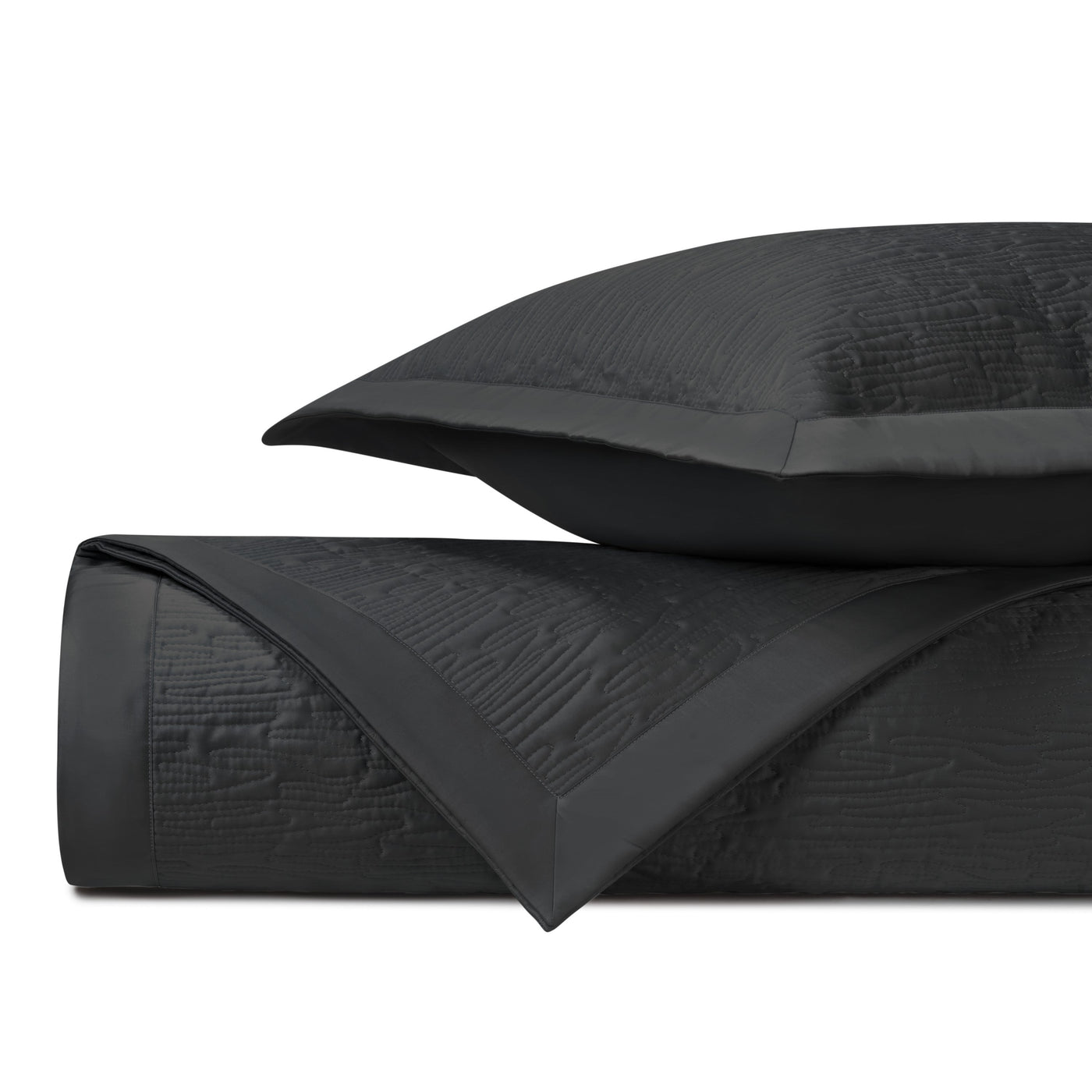 Close-up of black quilted coverlet and sham with geometric wave texture and satin border trim.