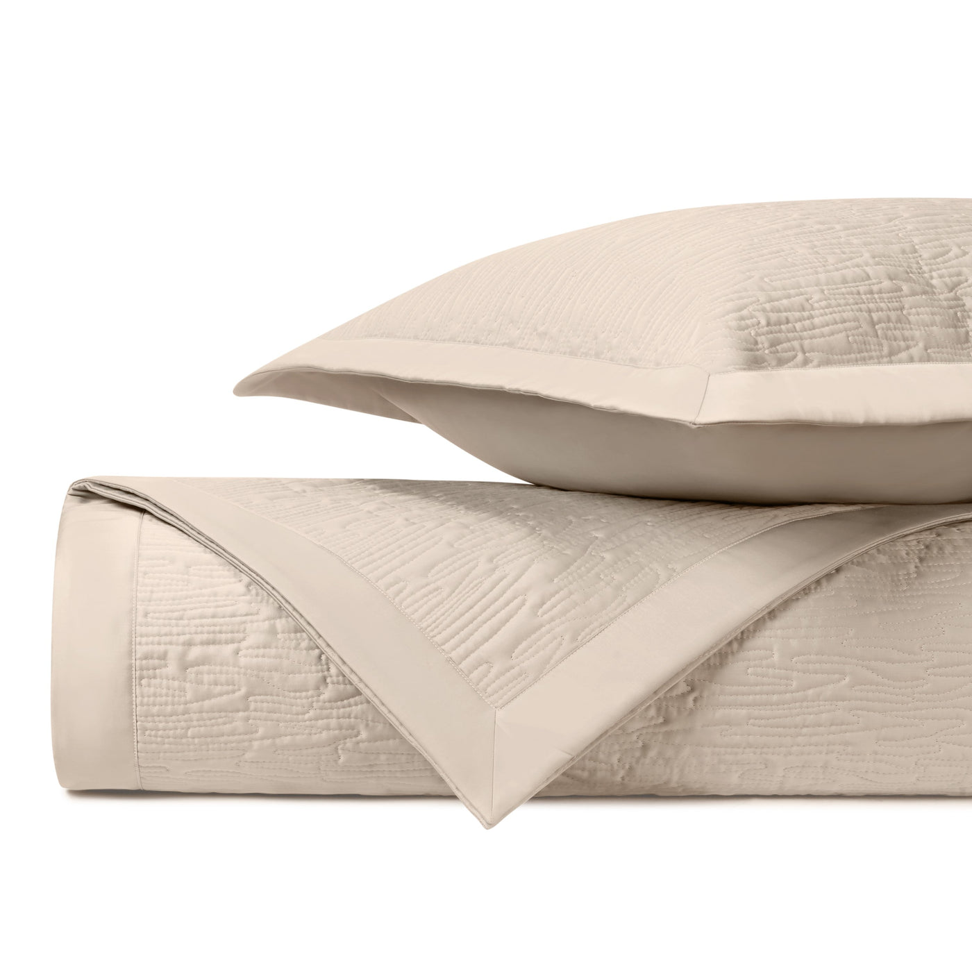 Ivory quilted coverlet folded with sham, showing textured wave-pattern stitching detail.