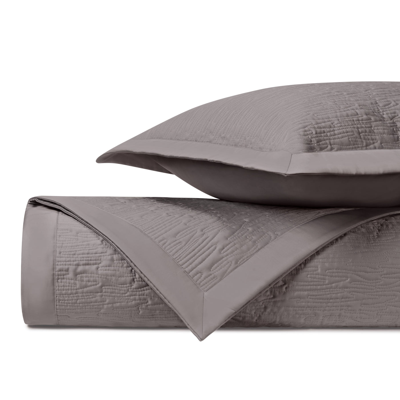 Close-up of taupe quilted coverlet with textured wave pattern and flat border edge.