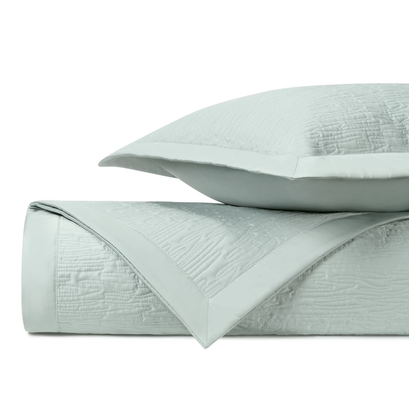 Close-up of mist blue quilted coverlet with textured wave pattern and satin border trim.
