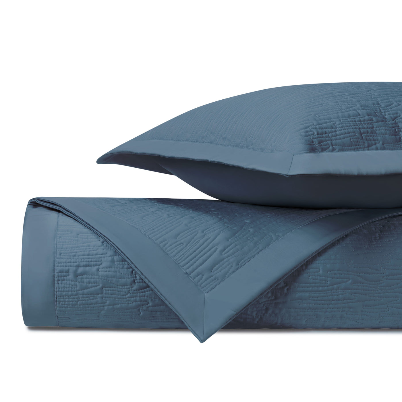 Close-up of slate blue quilted coverlet with textured wave pattern and matching sham.