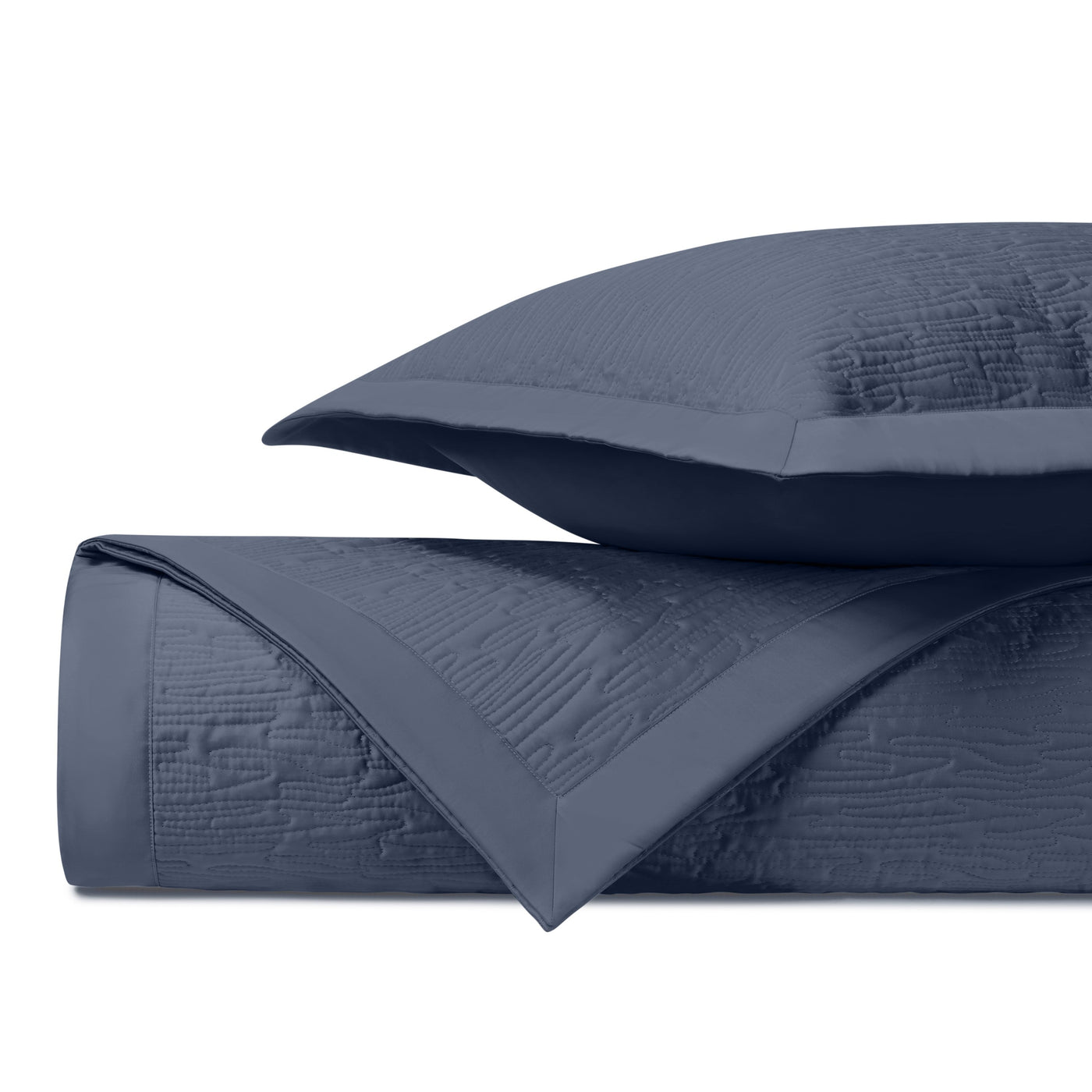 Navy quilted coverlet rolled beside a matching sham, showing textured wave pattern detail.