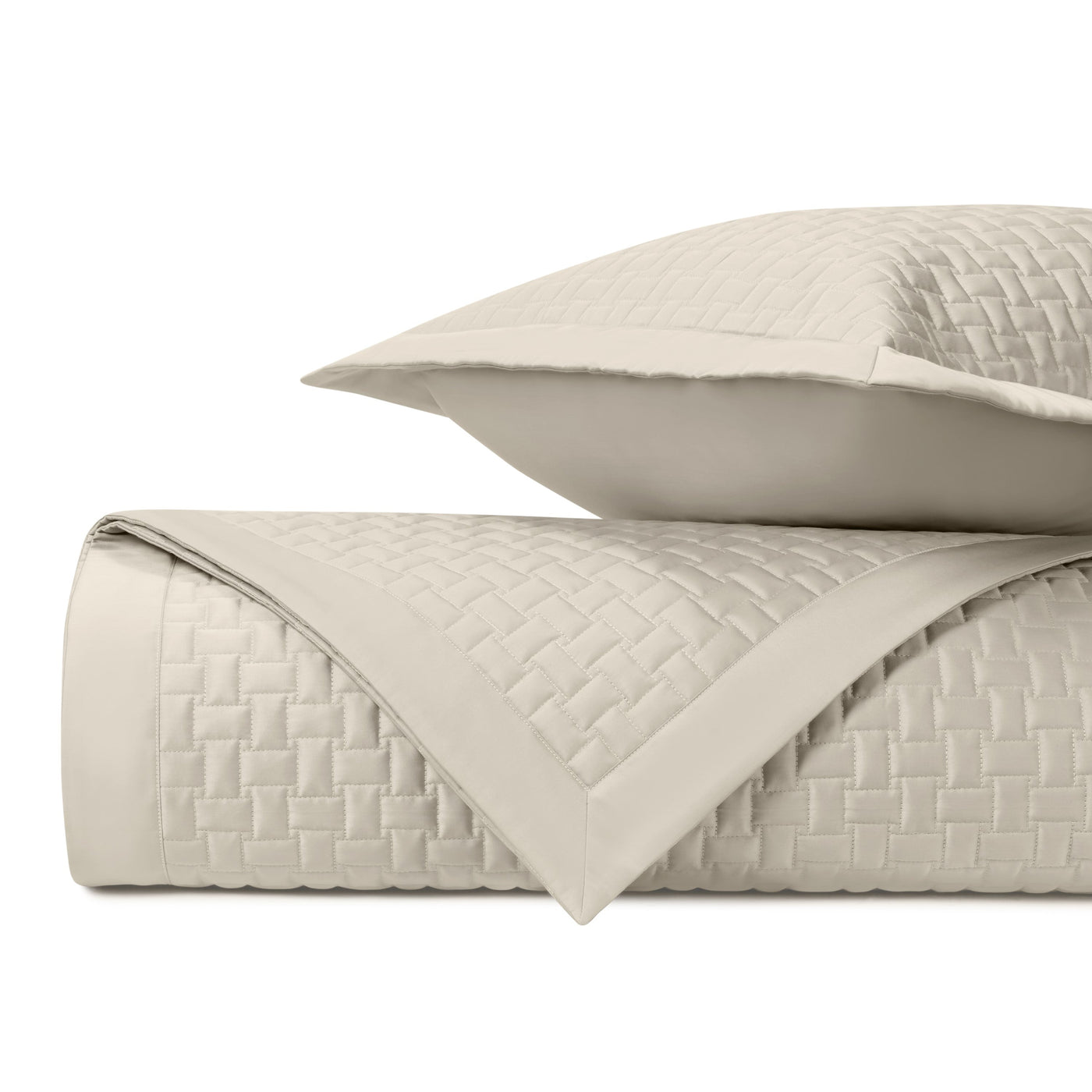 Close-up of ivory quilted coverlet with basket-weave texture and matching sham, folded and stacked.
