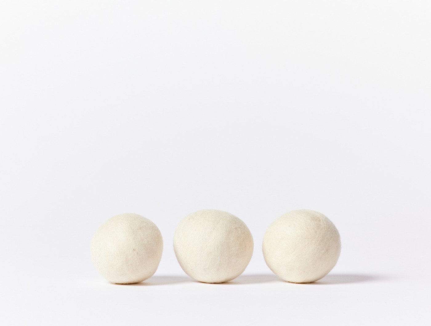 Coyuchi Felt Dryer Ball Set, three ivory wool balls on white background.