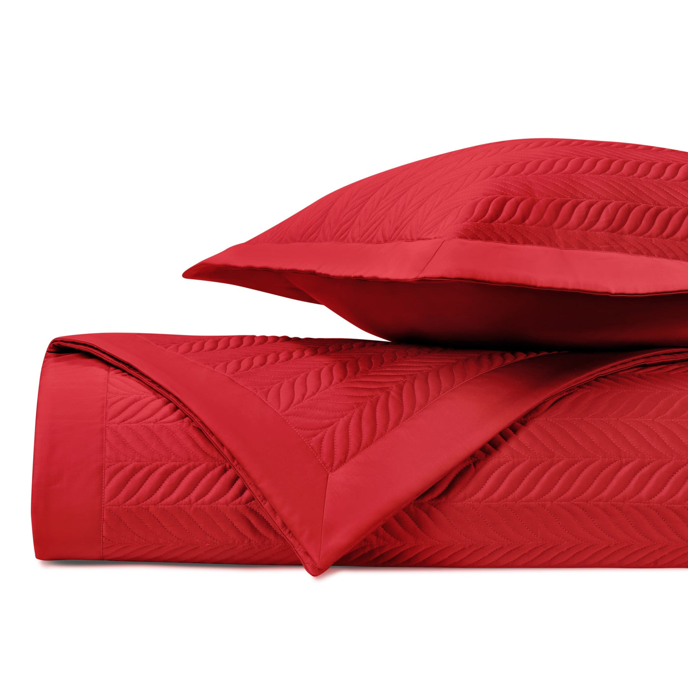 Crimson quilted coverlet rolled beside a sham, showing leaf-pattern stitching detail.