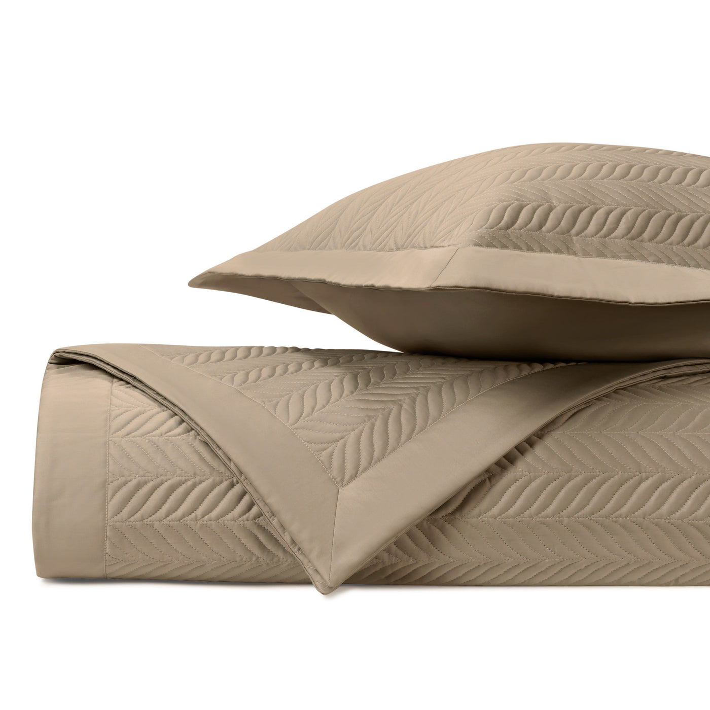 Close-up of wheat quilted coverlet and sham with tonal leaf-pattern stitching, neatly rolled and stacked.
