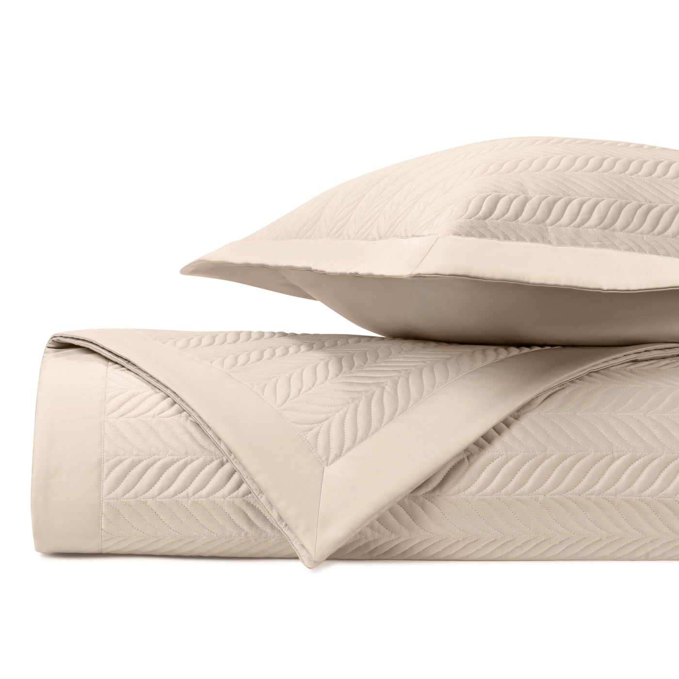 Close-up of ivory quilted coverlet with leaf motif stitching, folded with matching sham.