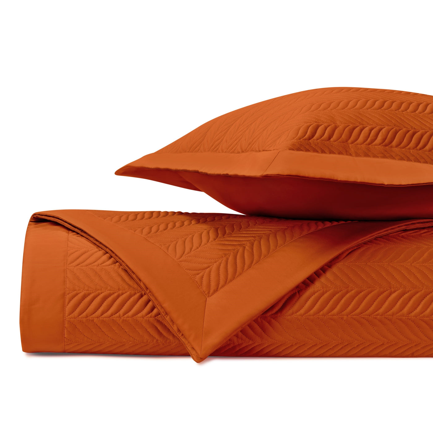 Close-up of quilted leaf-motif stitching on a tangerine coverlet and sham set.