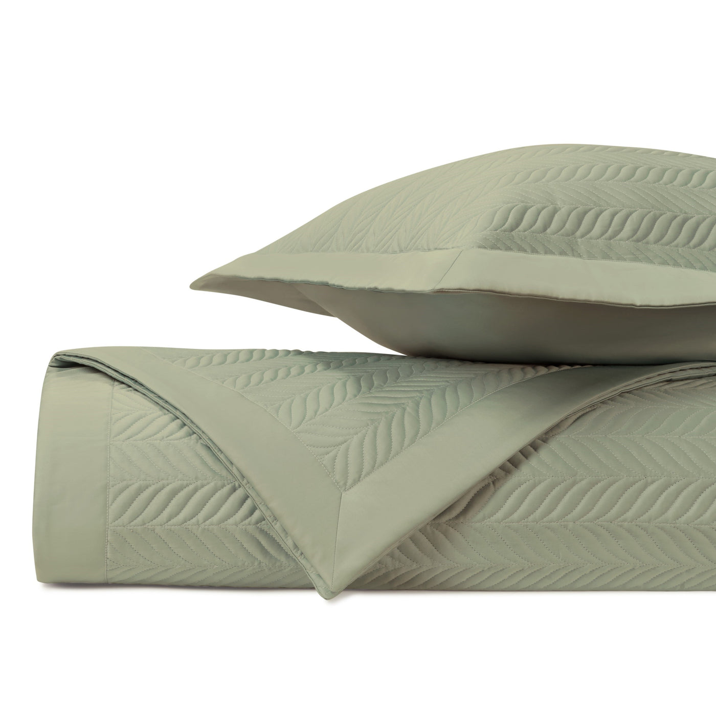 Close-up of sage green quilted coverlet with leaf motif stitching and matching sham.
