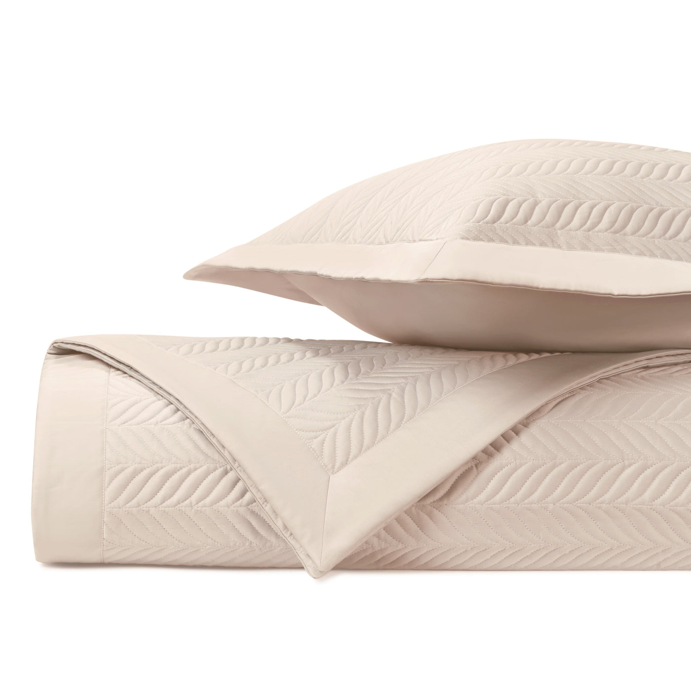 Close-up of blush quilted coverlet with leaf motif stitching, rolled beside matching sham.