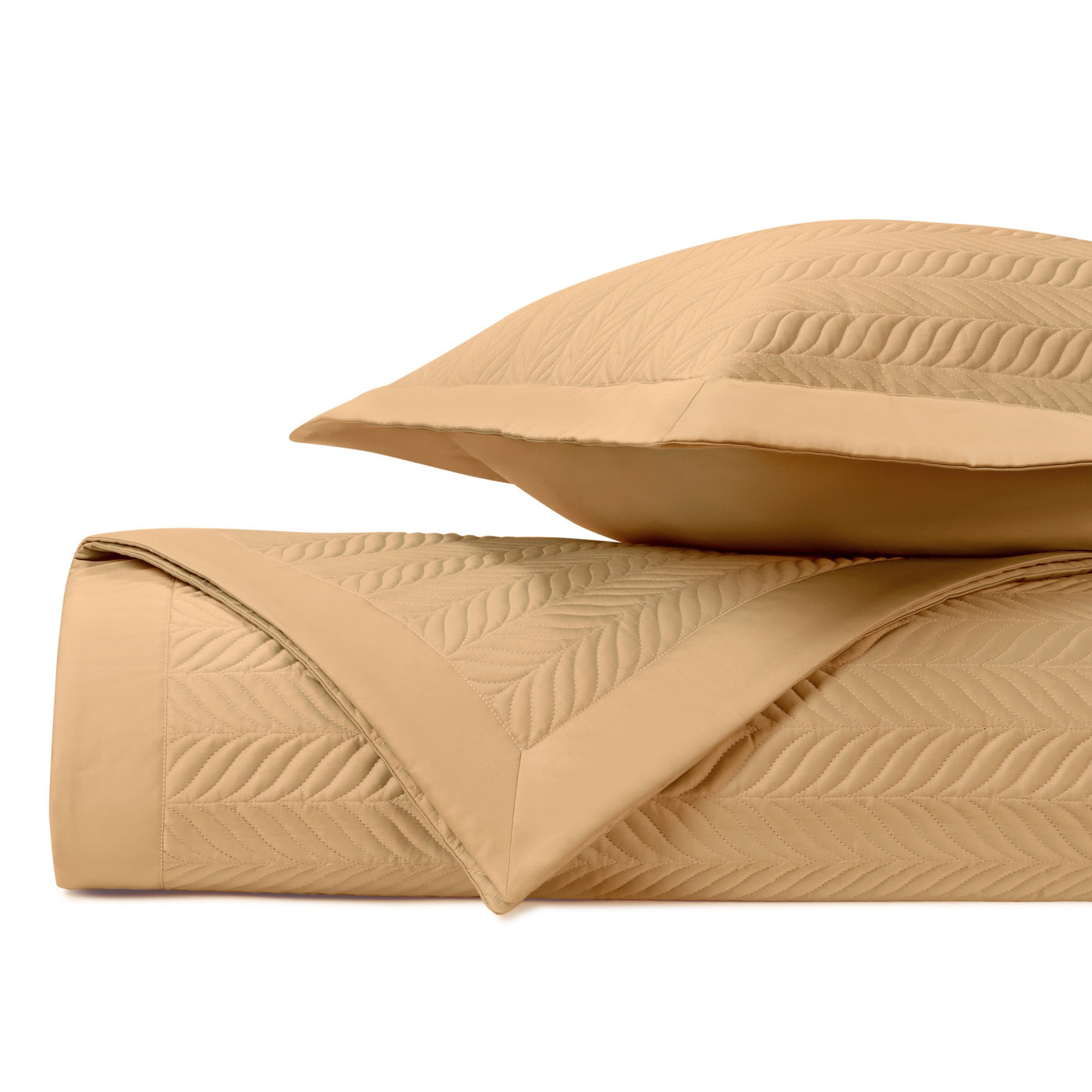 Rolled coverlet and sham in caramel, showing quilted leaf-pattern stitching detail.