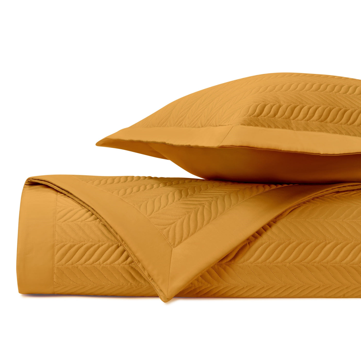 Close-up of marigold quilted coverlet and sham with embossed leaf pattern, neatly folded.
