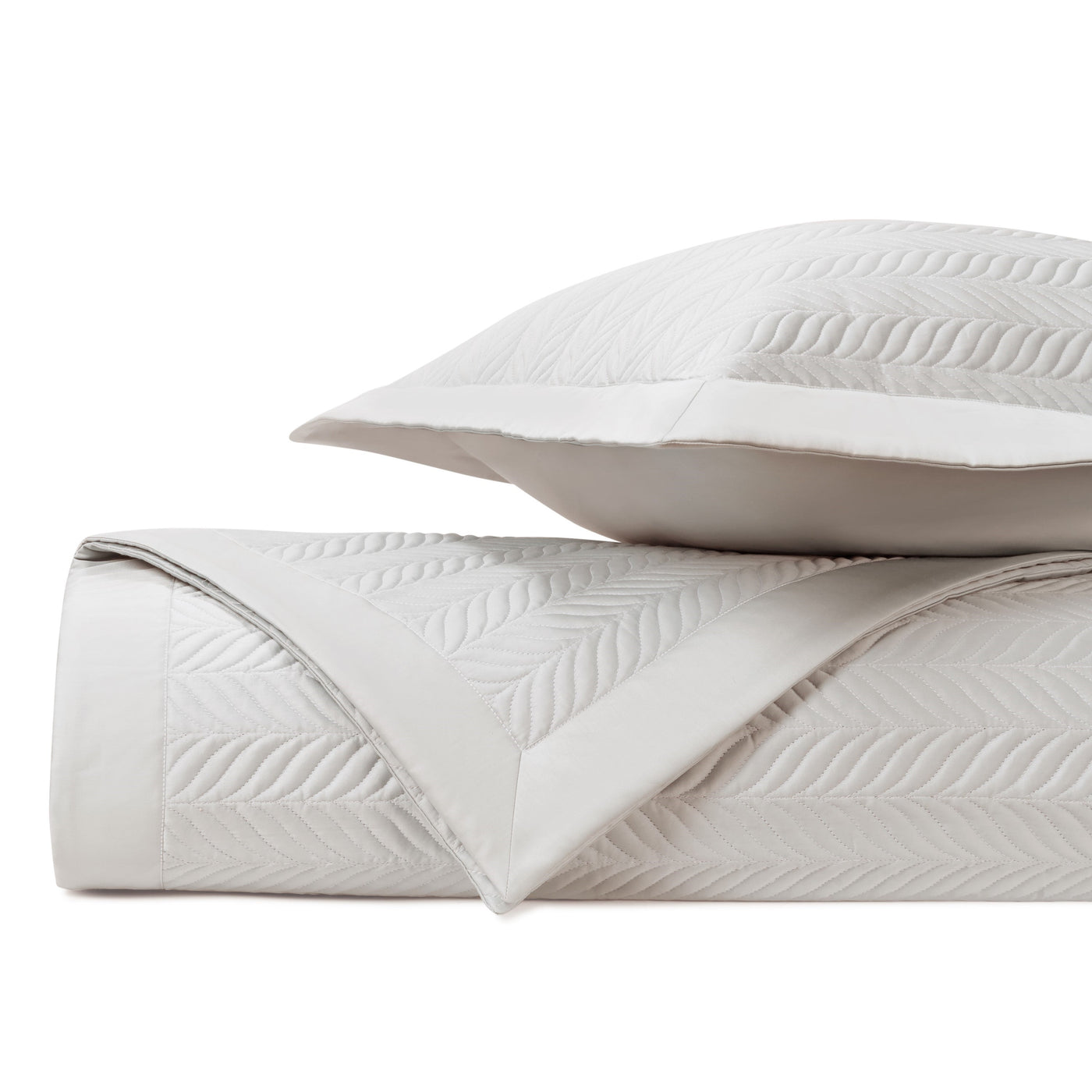 Close-up of ivory quilted coverlet folded edge showing herringbone leaf stitching pattern.