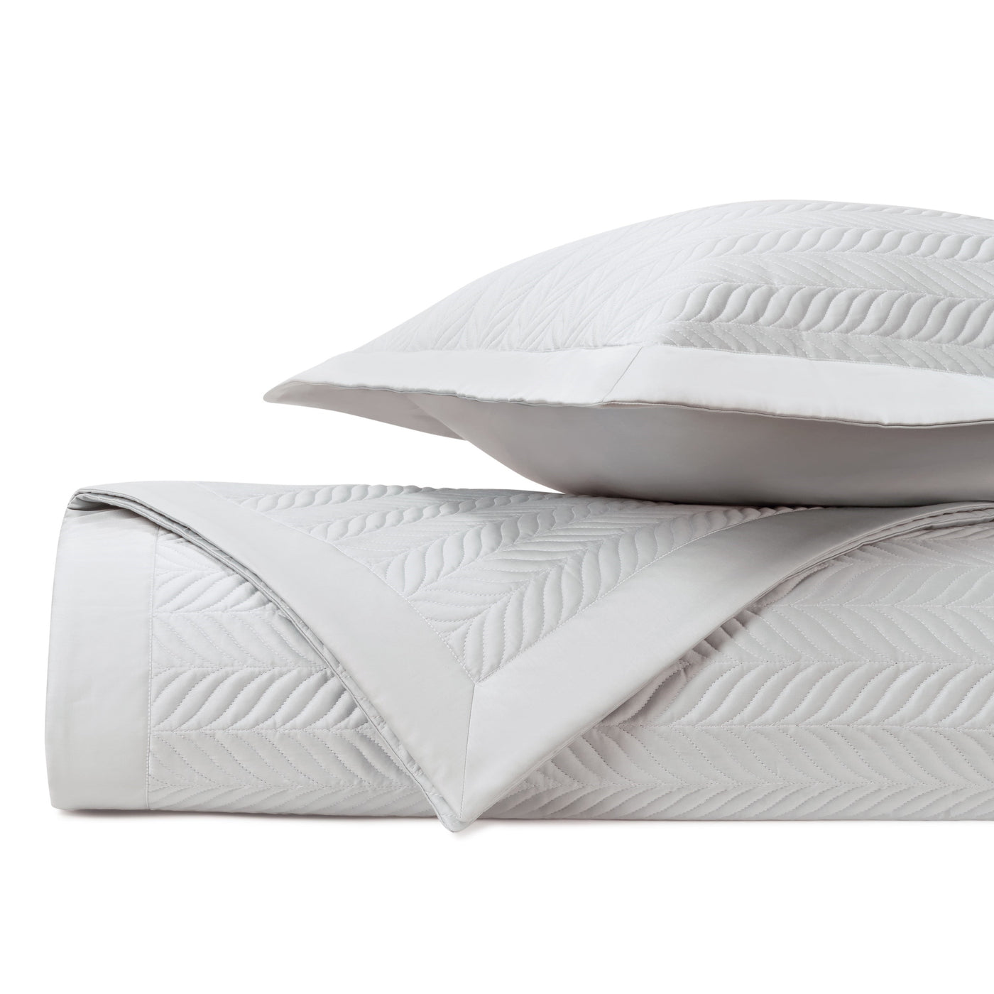 Rolled coverlet edge detail showing embossed leaf quilting pattern in white.