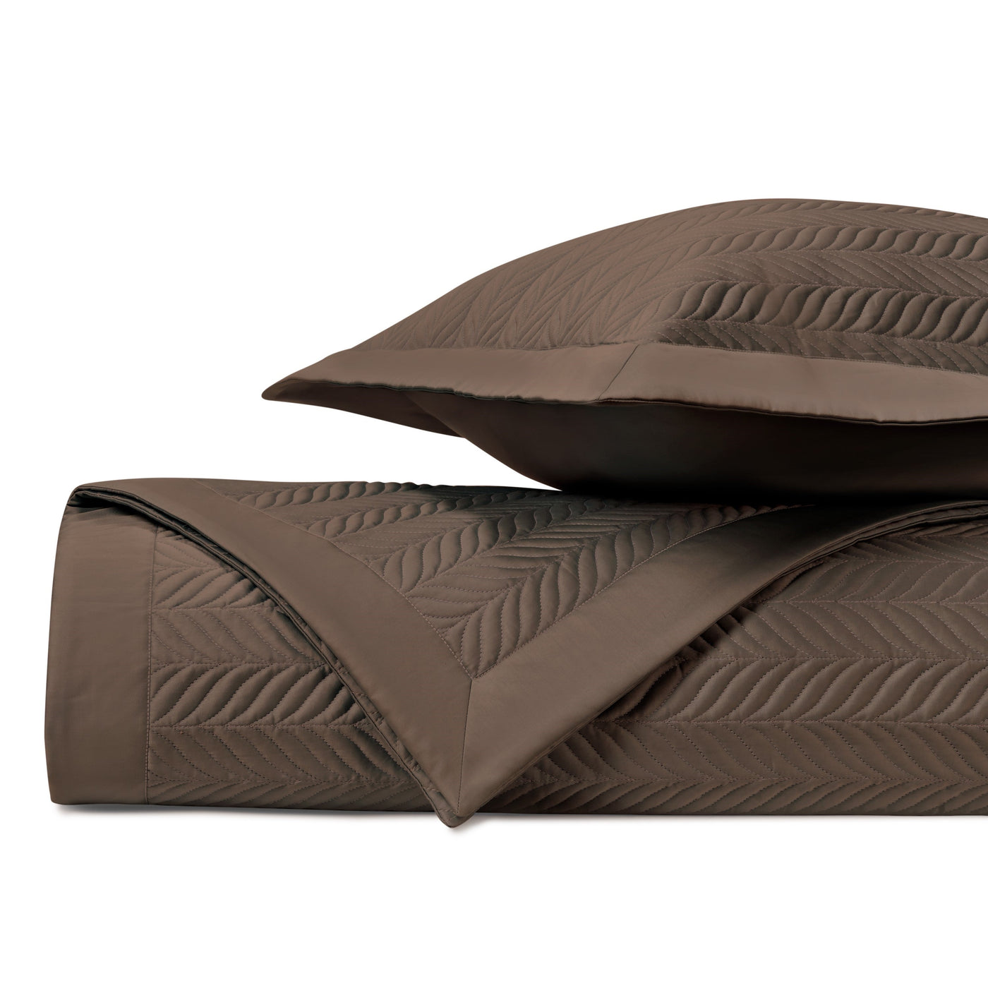 Close-up of chocolate quilted coverlet rolled beside a matching sham with leaf stitching.