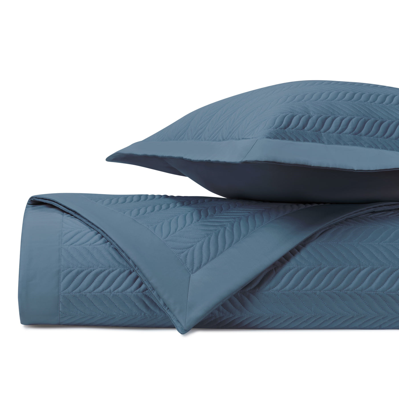 Folded slate blue quilted coverlet showing embossed leaf pattern stitching, with matching sham.