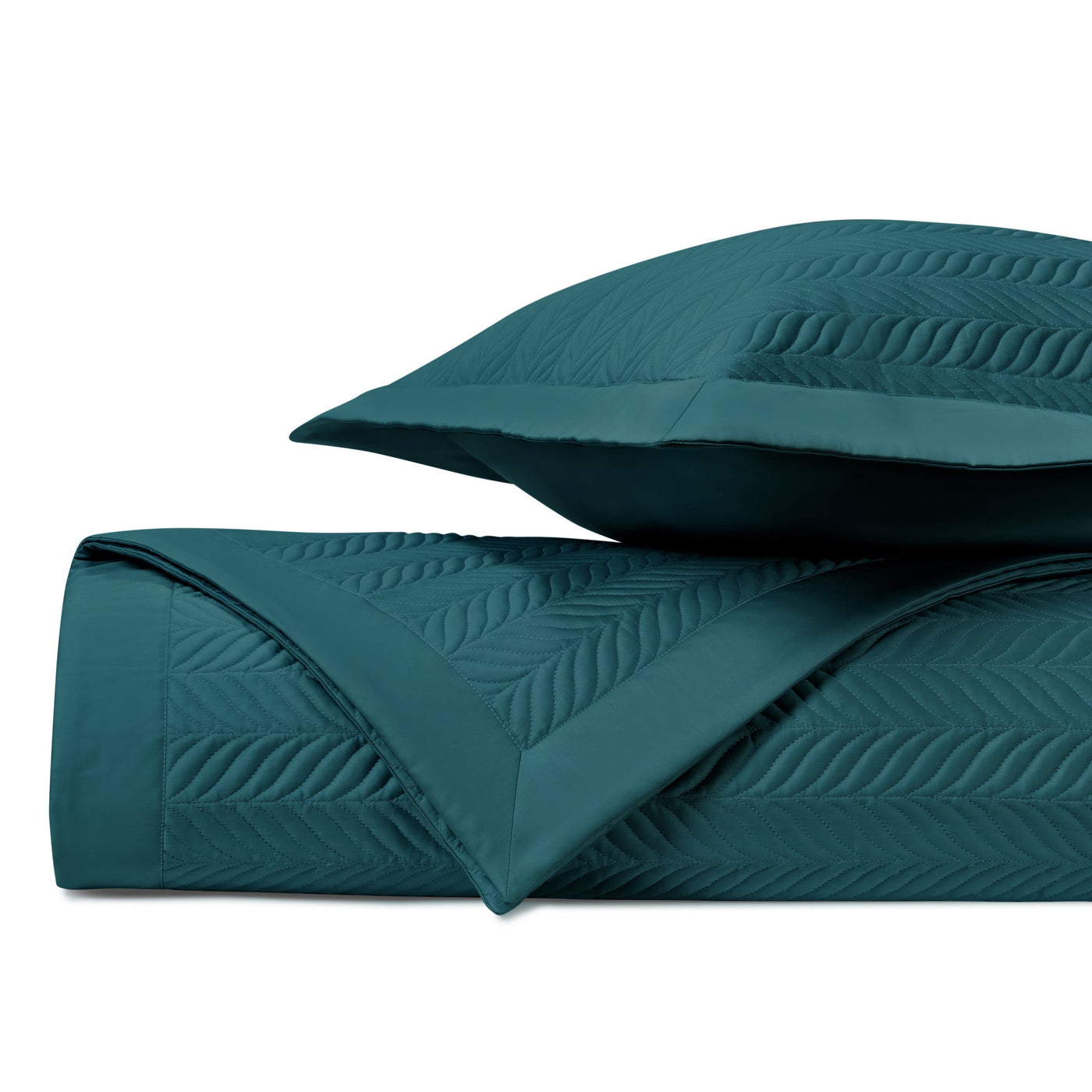Folded teal quilted coverlet with leaf-motif stitching and matching sham, studio shot.