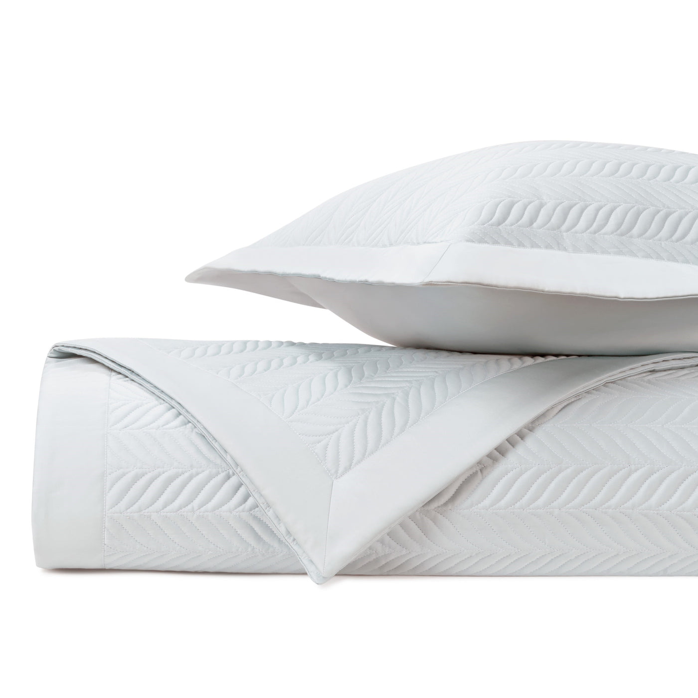 Close-up of white quilted coverlet and sham with raised leaf and herringbone pattern.