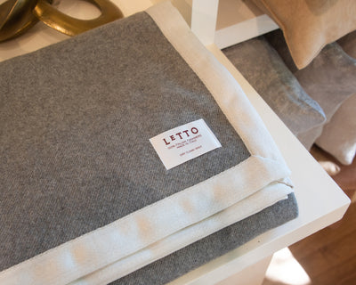 Letto Alpina blanket in heather grey with ivory border, folded on white surface.