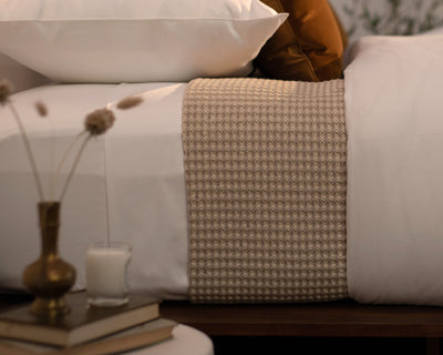 LETTO Nido blanket in taupe waffle-knit texture draped across white bed linens.